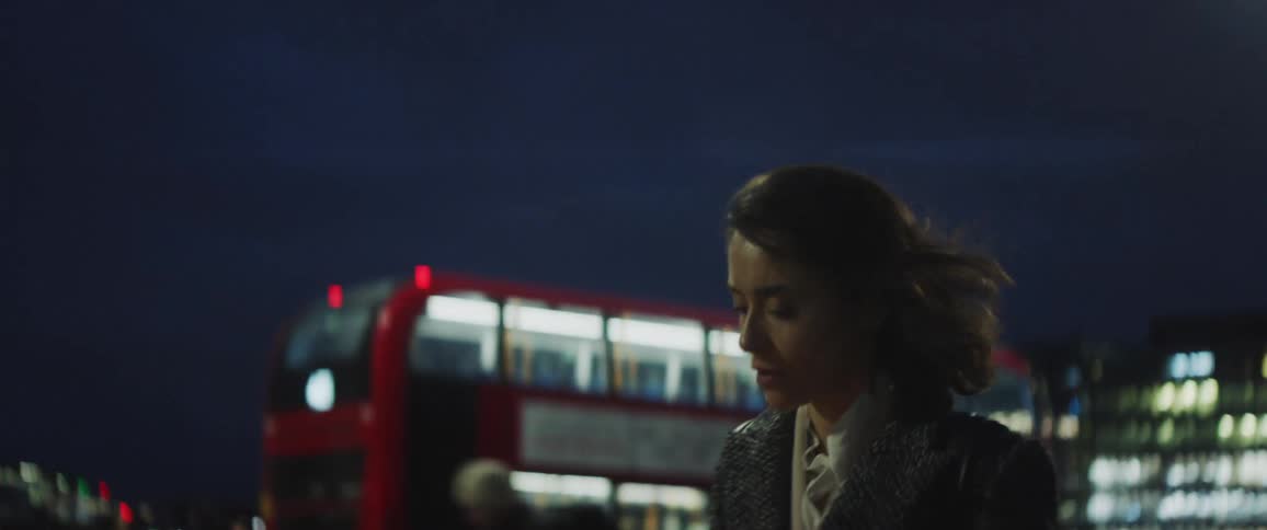 A young woman walks down a busy city street and looks at her phone as people walk past her