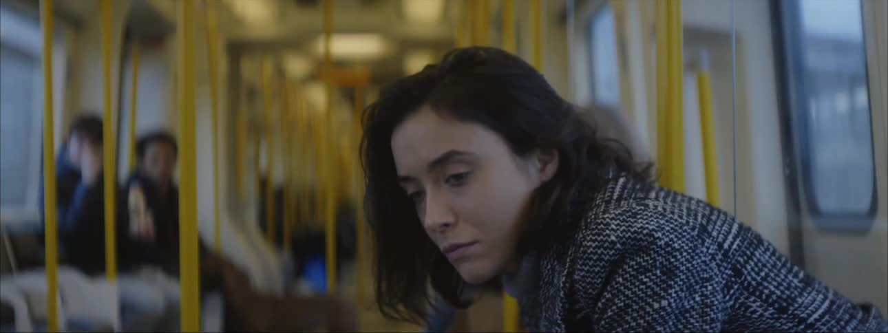 Woman with dark hair and dark gray coat sits on train traveling