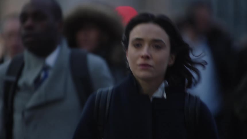 Woman with dark hair and gray overcoat walks in crowd