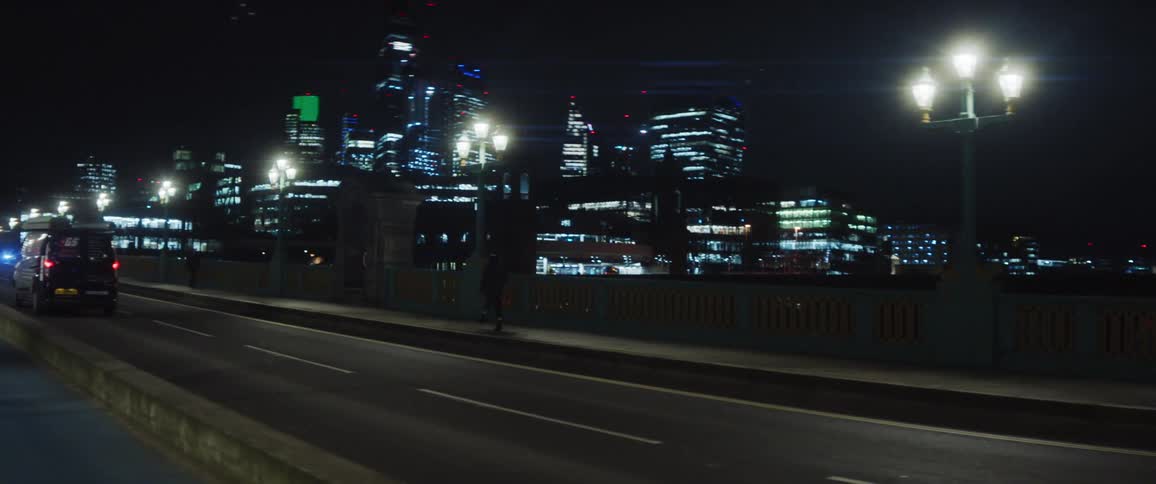 Female dancer dances on the bridge against he illuminated high rise buildings in the background at night