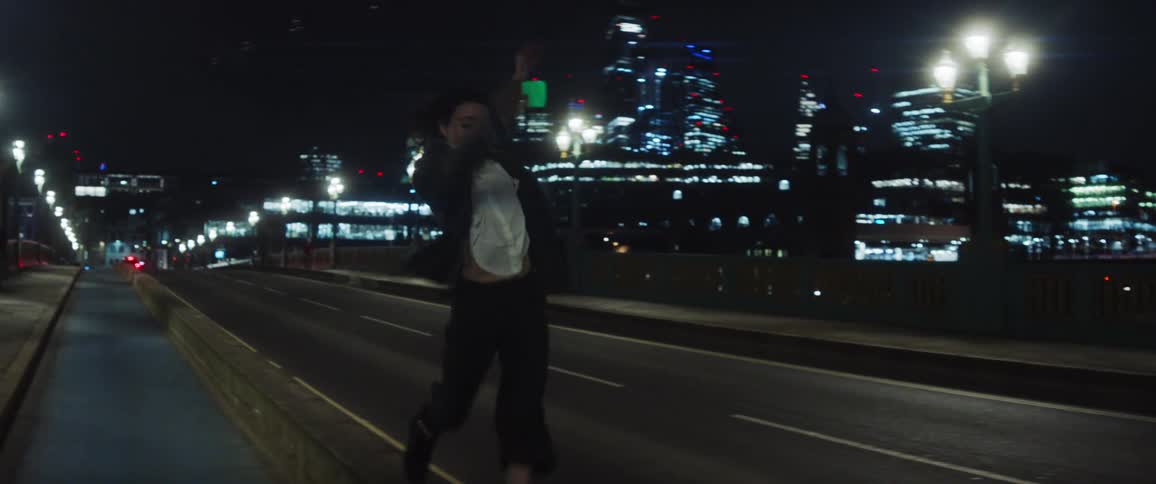 Young happy woman dances while running over a bridge near the city at night