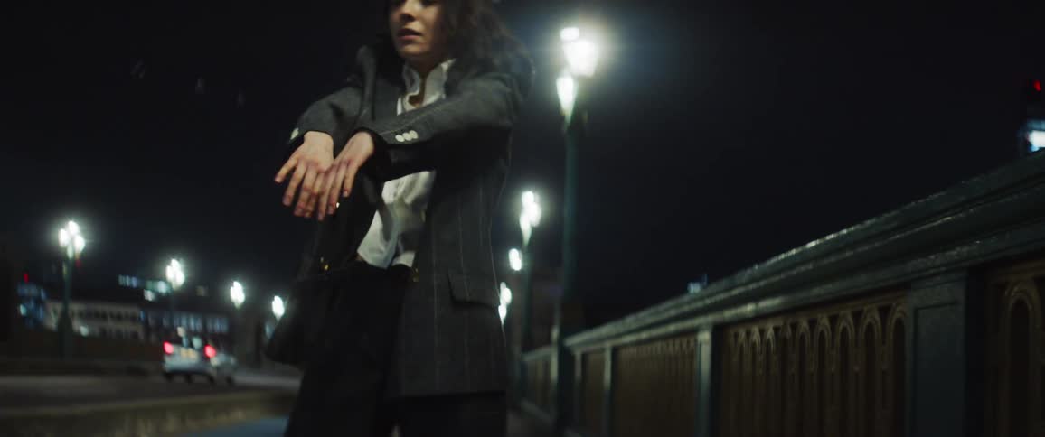 Woman with gray jacket and white shirt dances on the bridge at night