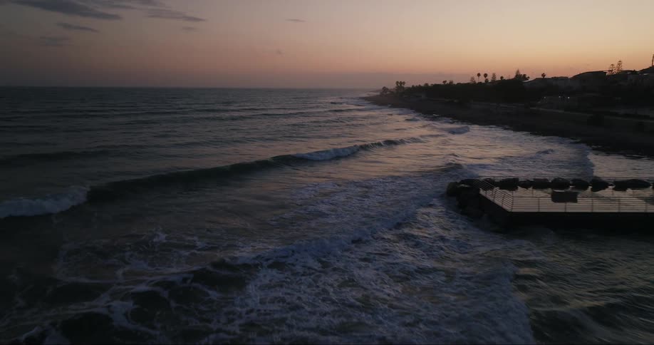 Aerial view of ocean waves breaking against the shore at sunset