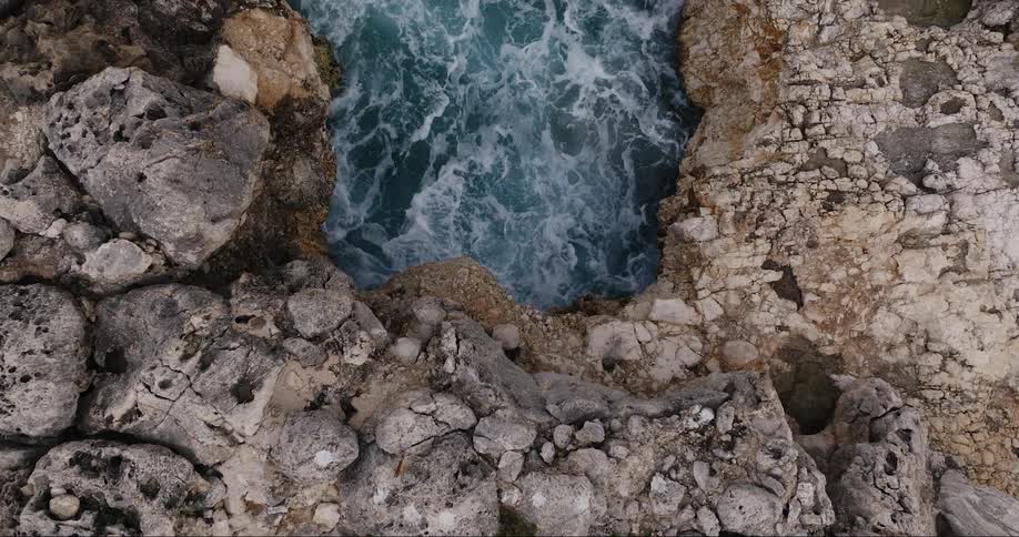Drone view of water crashing against a rocky coastline