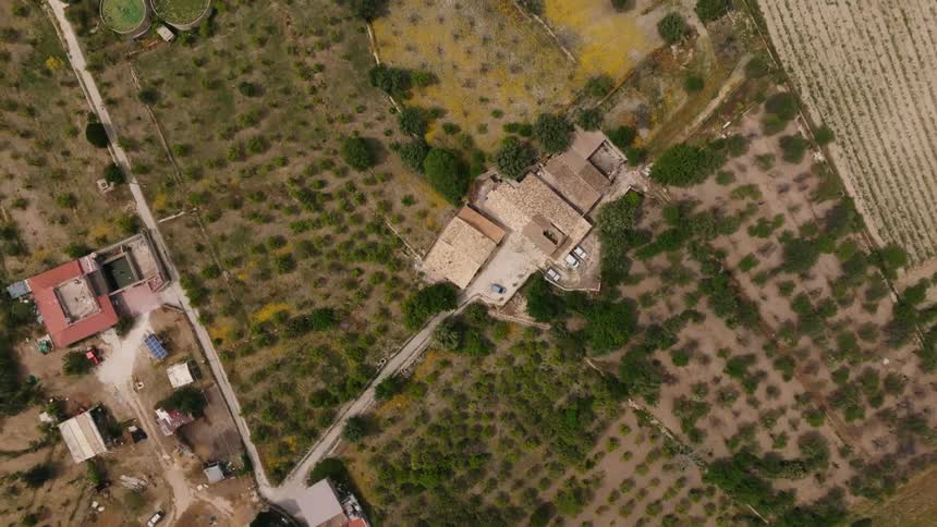 Automobiles are parked at a property that appears to be damaged with a hole in the roof in the middle of rural farmland with houses far apart