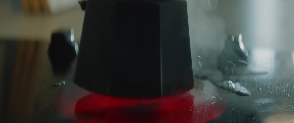 Close up of a black kettle on a flat stove element as it steams and simmers before a person takes it off