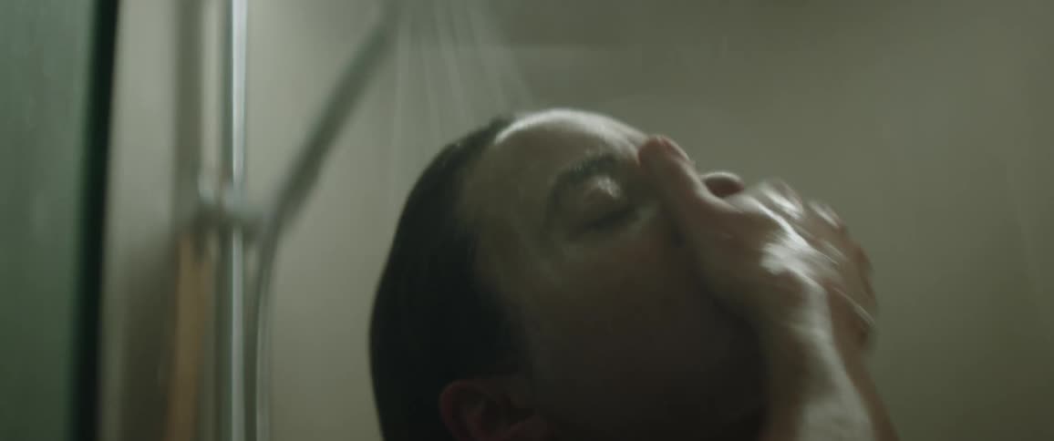 A woman is standing in the shower rubbing her hands over her face and eyes as she washes herself