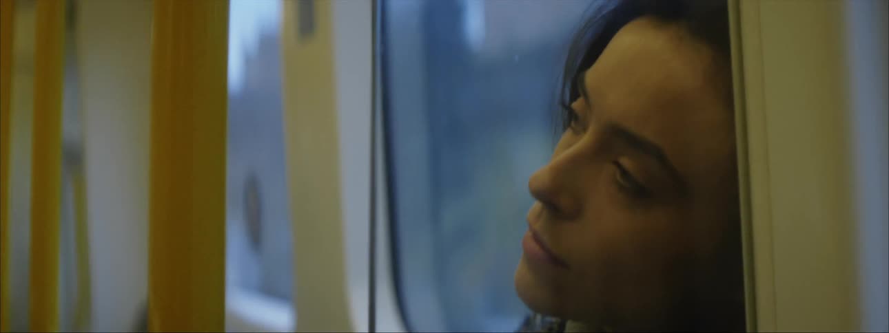 The view is of a young woman that is on a city bus in the day time