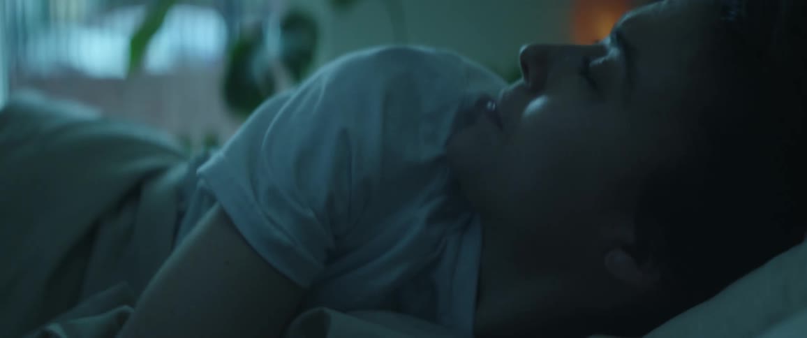 A close up of a womans face as she lays in bed looks around then rolls back over grabbing the covers