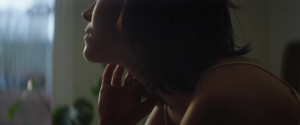 A close up of a woman sitting with her head on her hand then rubbing her face