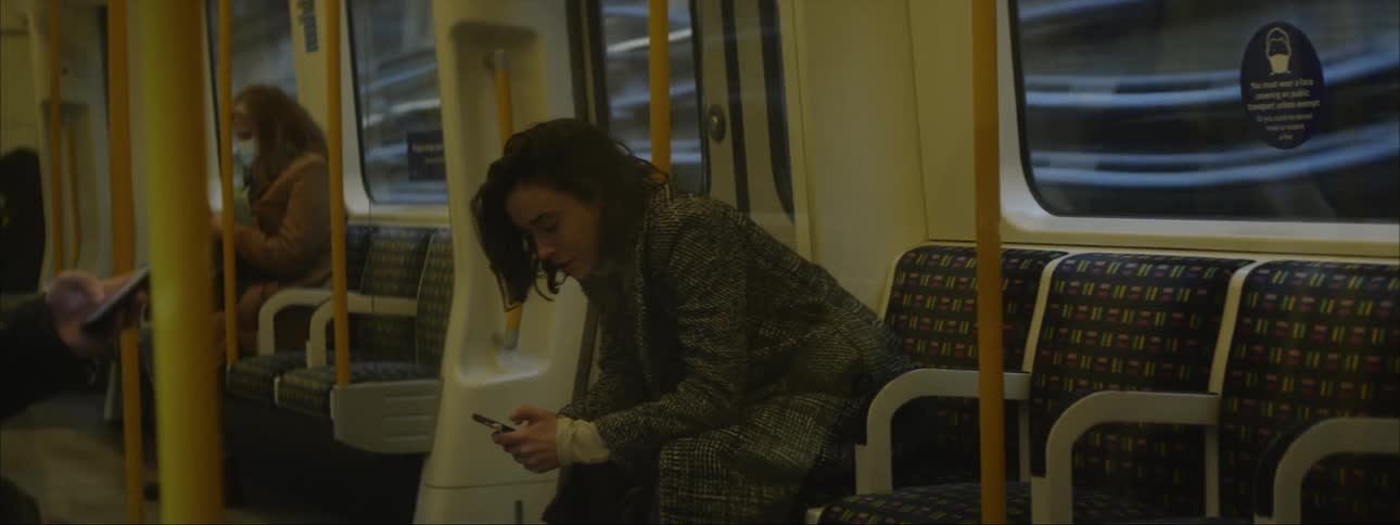 A woman is sitting on a train texting on her phone as it travels through the subway and the man sitting across from her has his phone in his hand