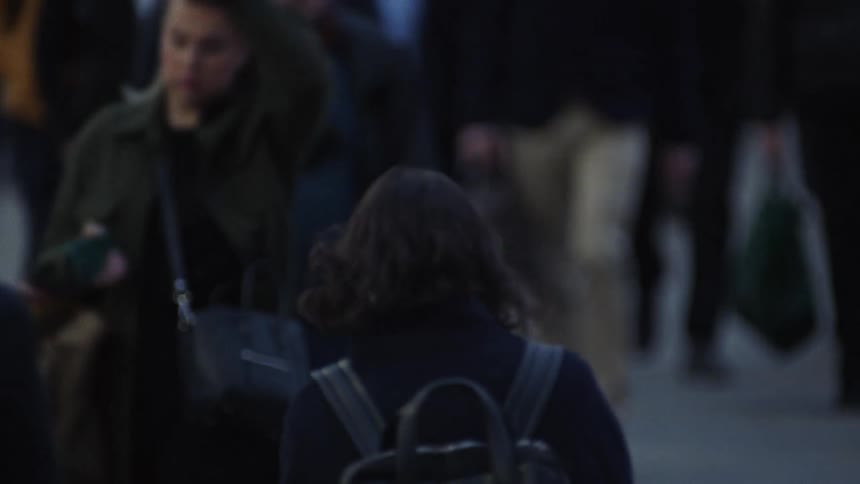 Woman with backpack walks in opposite direction of crowd of pedestrians all wearing coats
