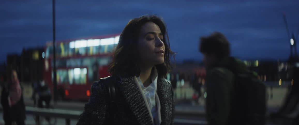A young woman stands on a busy city street with her eyes closes as people walk past