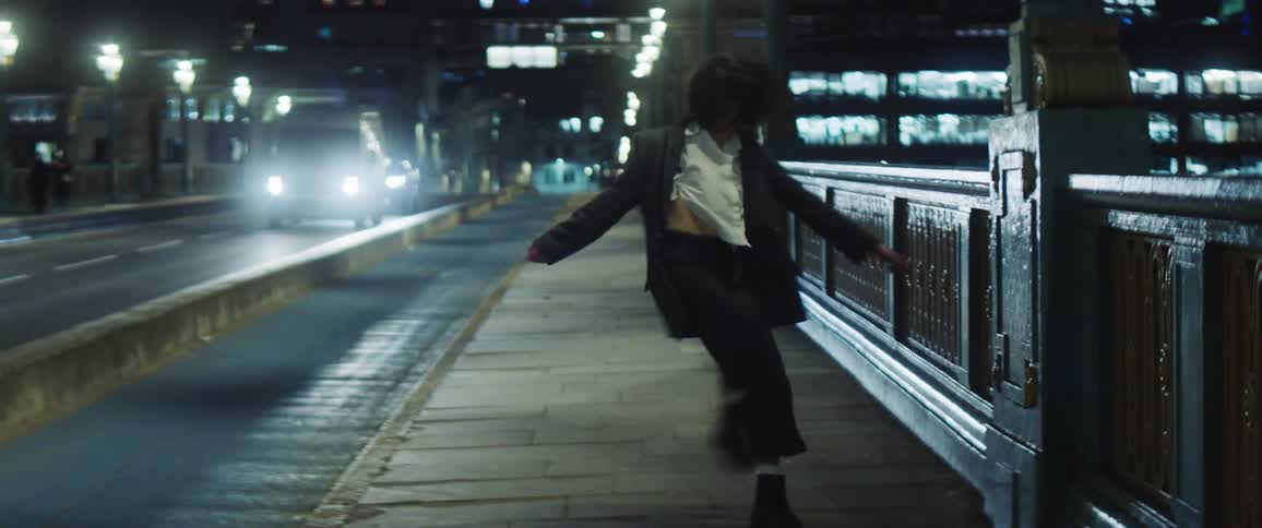 A young woman dances on a city street as cars drive past