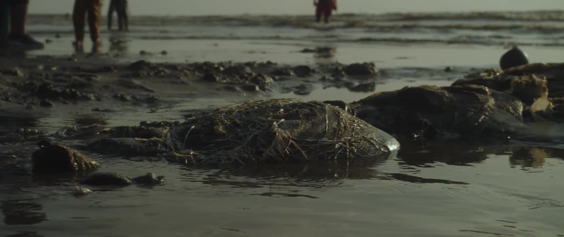 People stand on a river bank littered with trash