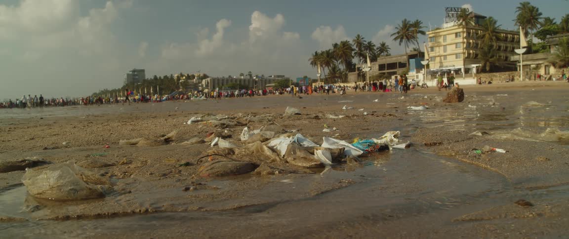 Garbage on a beach as crowds of people are gathered near the buildings