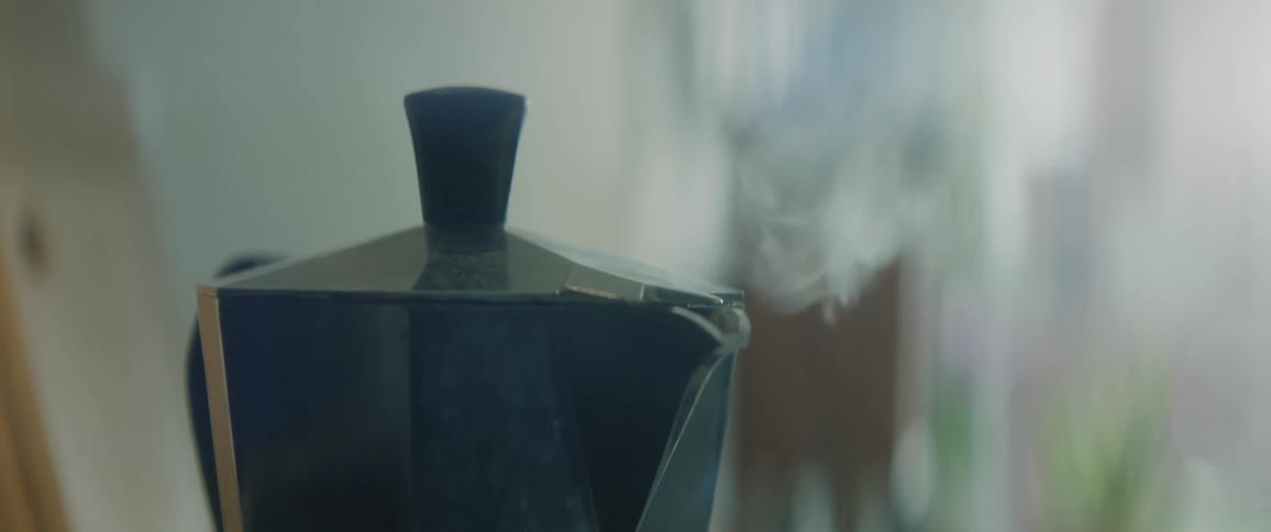 Italian moka sitting on stove steaming coffee is ready and someone lifts the lid to see if its full