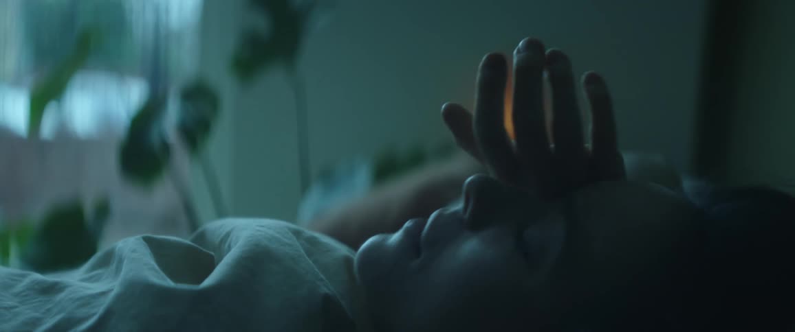 A close up of a woman laying in bed looking around with her hand on her face