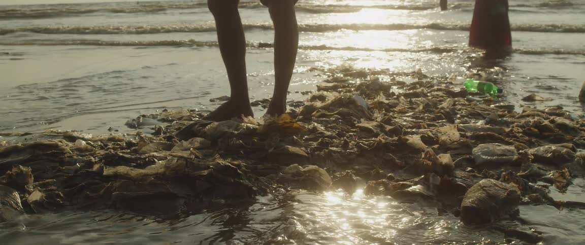 Reflection of a man walking near a puddle of sea water surrounded by garbage on the coast