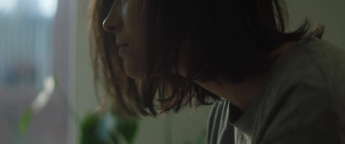 Woman sitting inside looking down then lifting her head up with her eyes closed