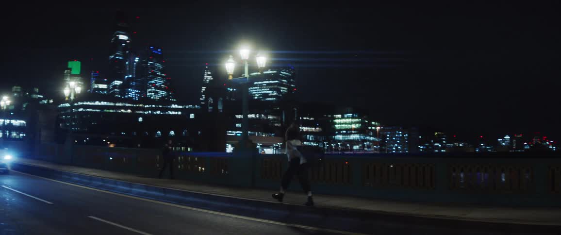 Woman walking along busy bridge near downtown at night takes off jacket and lifts it above her head as she runs