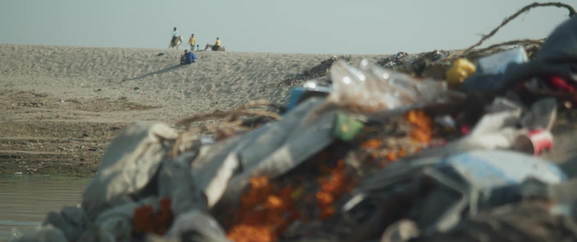 Garbage piled up on a sandy area near dirty water