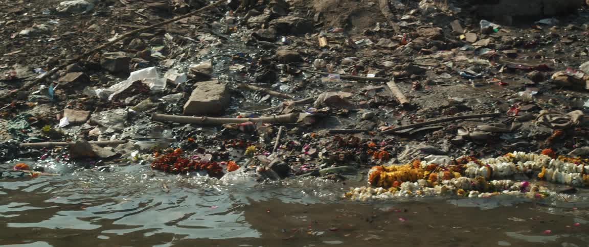 Close up of debris washing up on the shore of a river near a boat