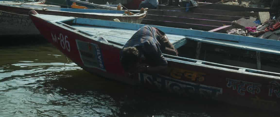 Man sitting in boat surrounded by flood or hurricaine damage and displaced people leans over boat and rinses face with water