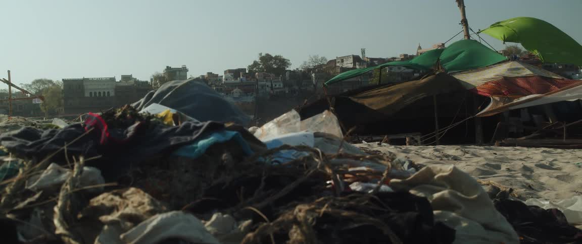Garbage piled up on a sandy beach with tents and canopies tied up near it