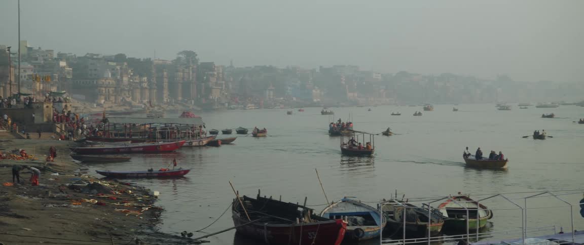 Several boats and barges travelling through a river in an indian city