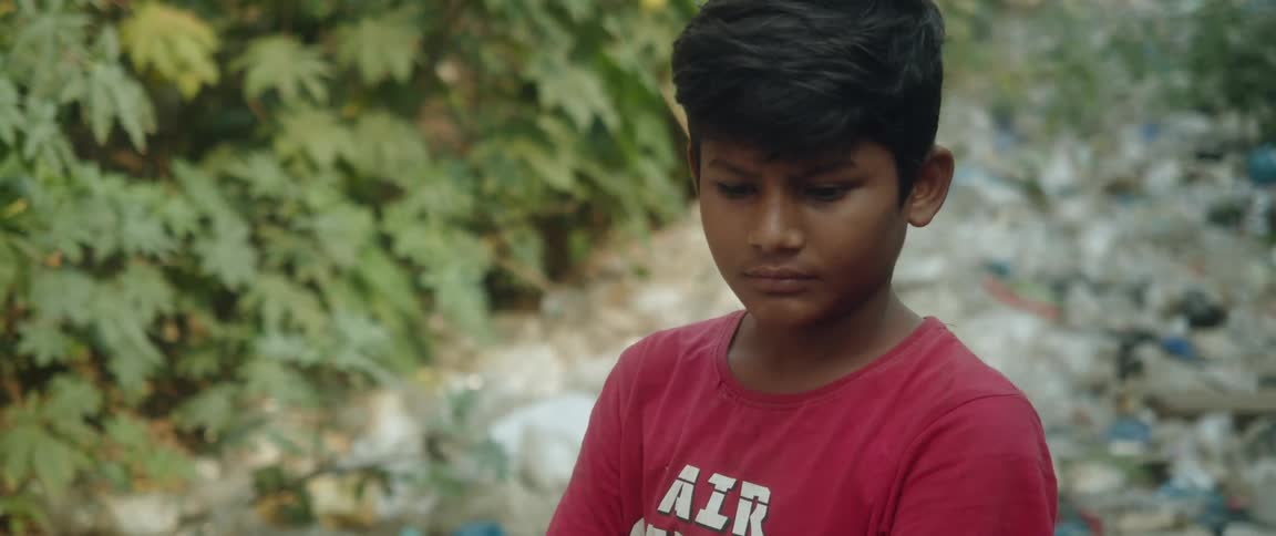 Boy with earring and red t shirt looks around near the dirty small river