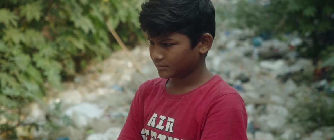 Young boy standing in a large pile of garbage outdoors while furrowing his brow