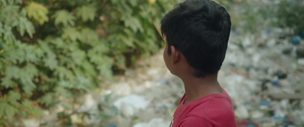 A close up of a young boy standing outside in a pile of garbage while looking around