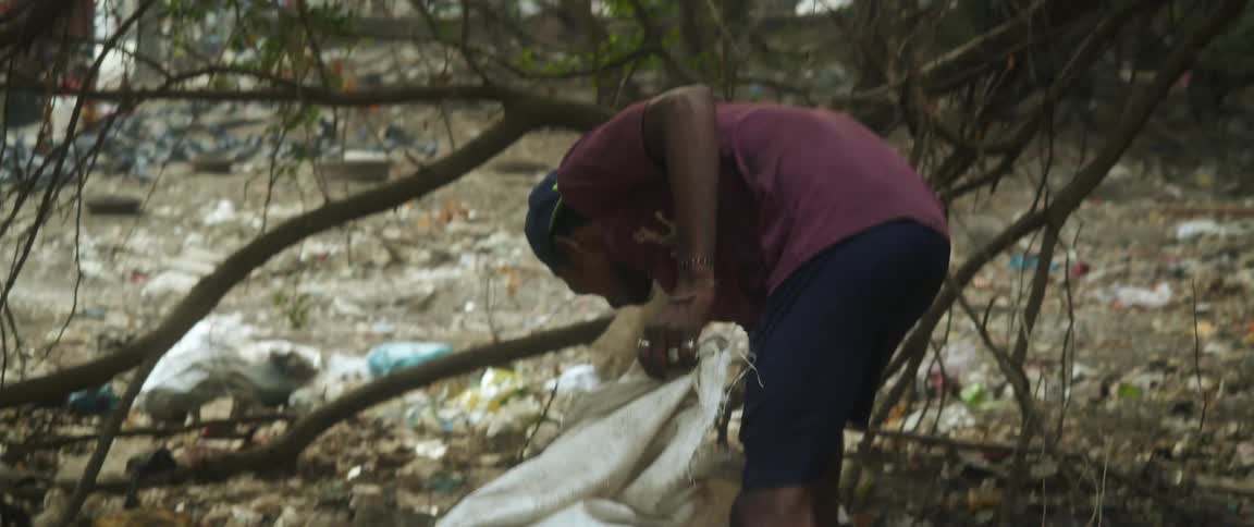 Man picks up plastic and other things from garbage strewn on ground