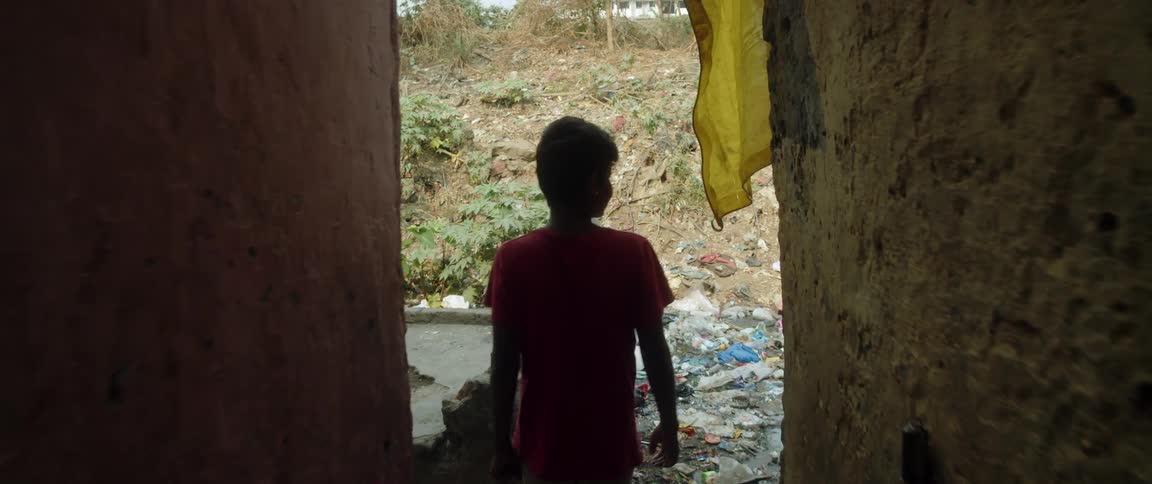 Young boy walking down long dark hallway and emerging outdoors where he finds the area flood damaged with water and trash scattered about