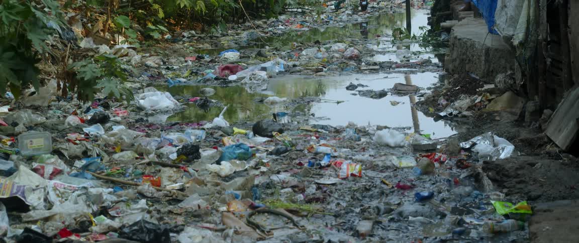 People stand on platform near trash covered brook containing reflective water