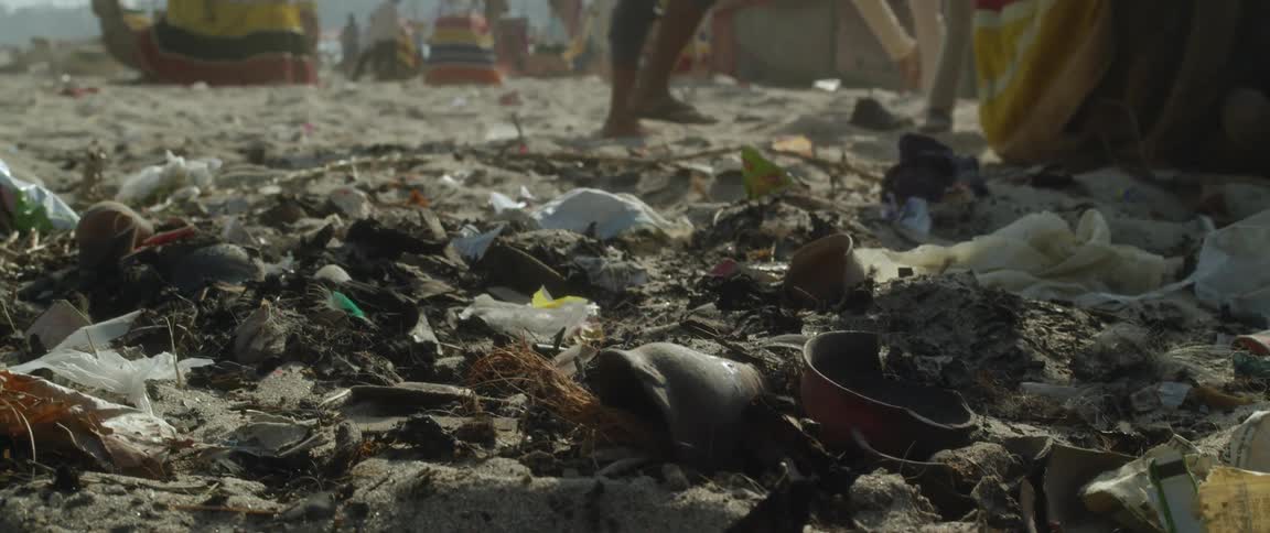 People walk across trash strewn ground with horse rider and camel in the background