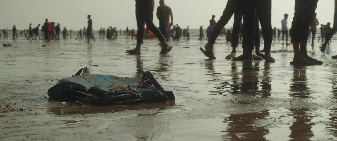 Crowds of people walking around on a wet beach as garbage is strewn about
