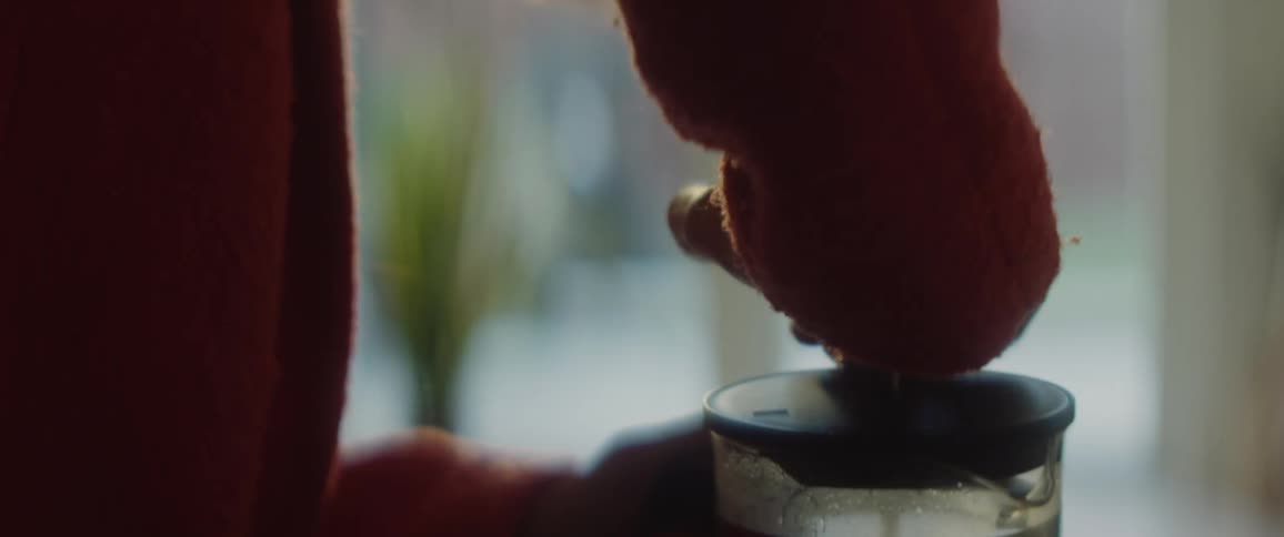 Woman with orange sweater uses french press to make coffee