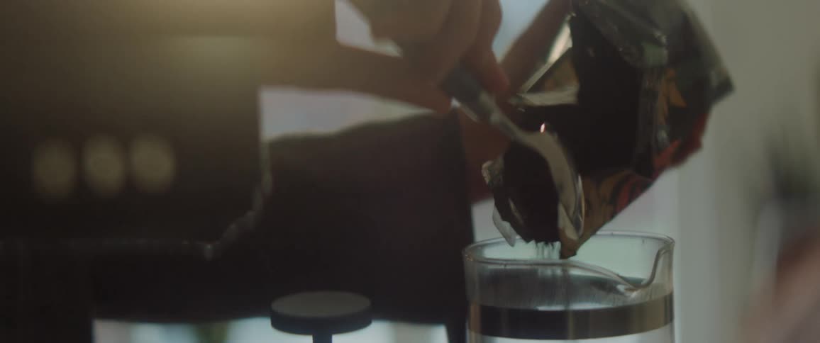 Silhouette of a person filling a french press with ground coffee at home