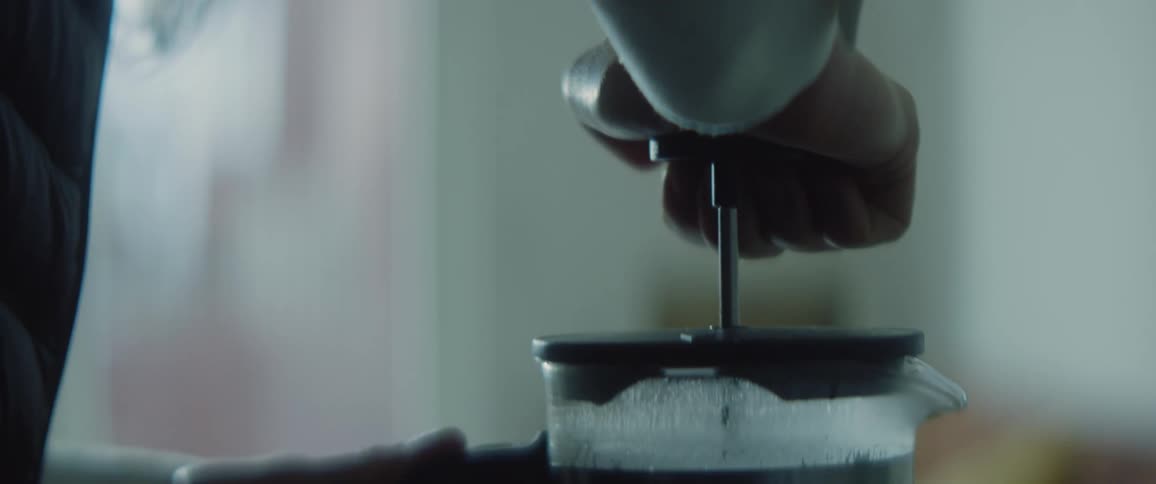 A woman pushes down on a plunger as she makes coffee
