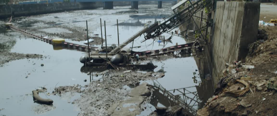 An improvised passageway over a shallow dirty river filled with trash