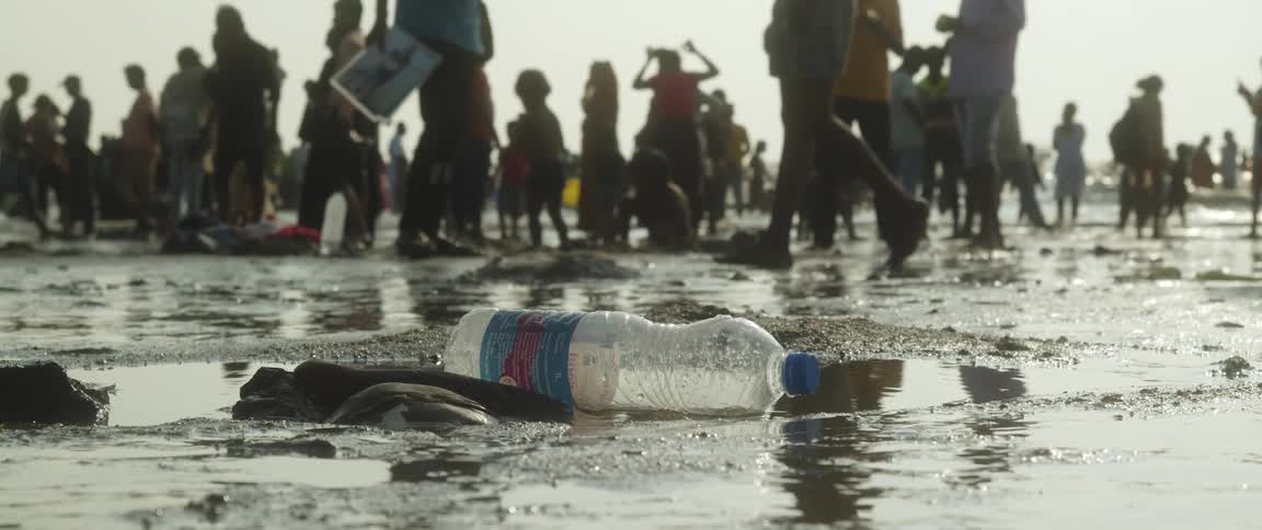 Close up of an empty plastic bottle over the wet sand near a crowd in the beach