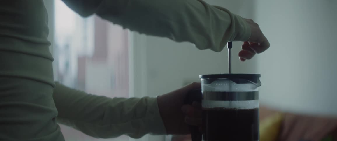 Person pressing a coffee press down in a glass carafe on their kitchen counter