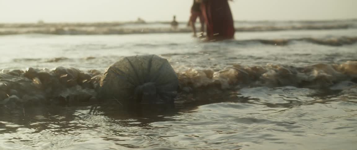 Waves roll into shore and people are wading in the water as a bag of garbage floats on the surface