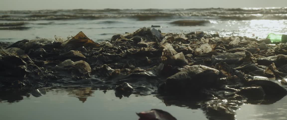 Garbage piled on a beach as waves roll onto the sand and people wade in the water