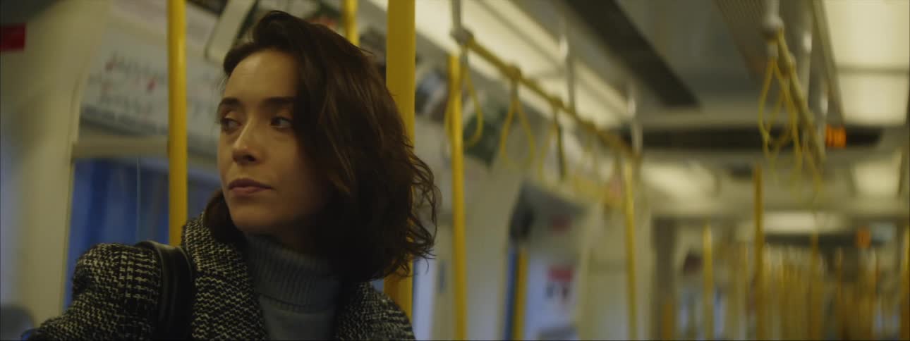 Close up of the face of a woman standing on a train moving thorugh the city