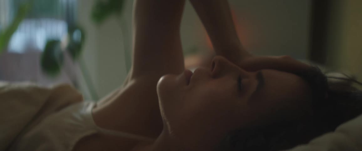 Close up of a woman laying in her bed with her hand on her head as she rolls over