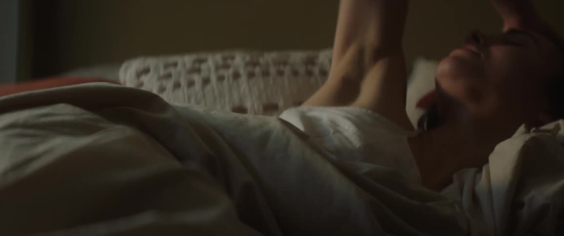 Woman in bed under covers is just waking up raises arm to stretch