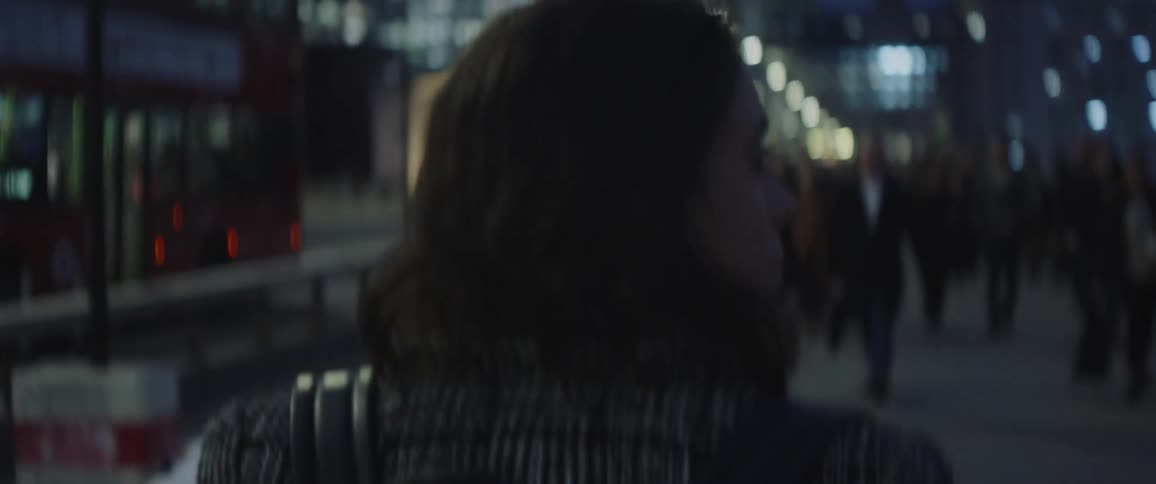 The backside of a woman walking down a city sidewalk as other people walk around her